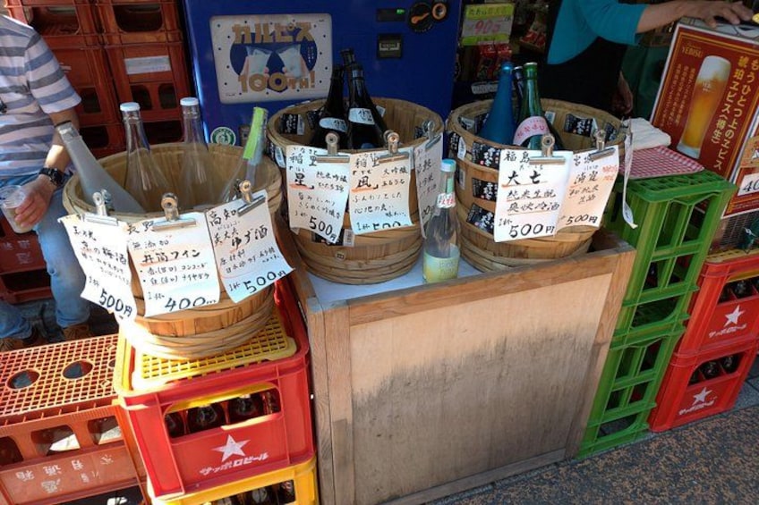 Eine Auswahl an Sake-Flaschen mit Preisschildern in einer Marktumgebung. 3