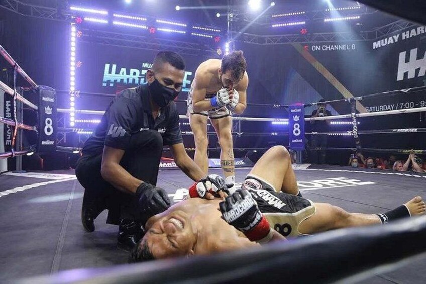 Un ring di boxe con una persona a terra, un'altra in piedi sopra di lei e un arbitro inginocchiato accanto. 2