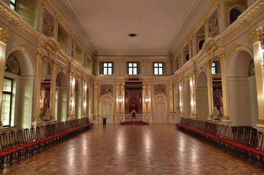 A grand hall with ornate columns, a long red carpet, and a central red throne. 5