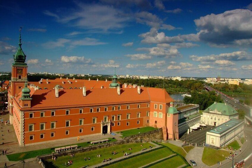 A large red brick building with a green tower, surrounded by green lawns and a clear blue sky. 2