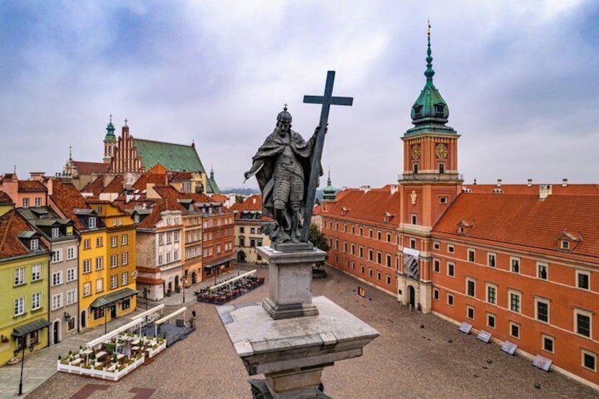 Una estatua de una figura histórica sosteniendo una cruz, rodeada de edificios coloridos y una torre con reloj. 4