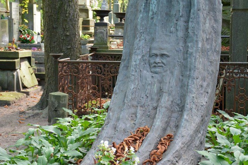 A tree with a carved face, surrounded by cemetery headstones and greenery. 3