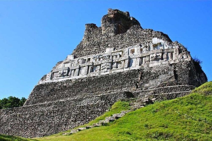 Una gran pirámide de piedra con intrincados grabados, rodeada de hierba verde y un cielo azul despejado. 2