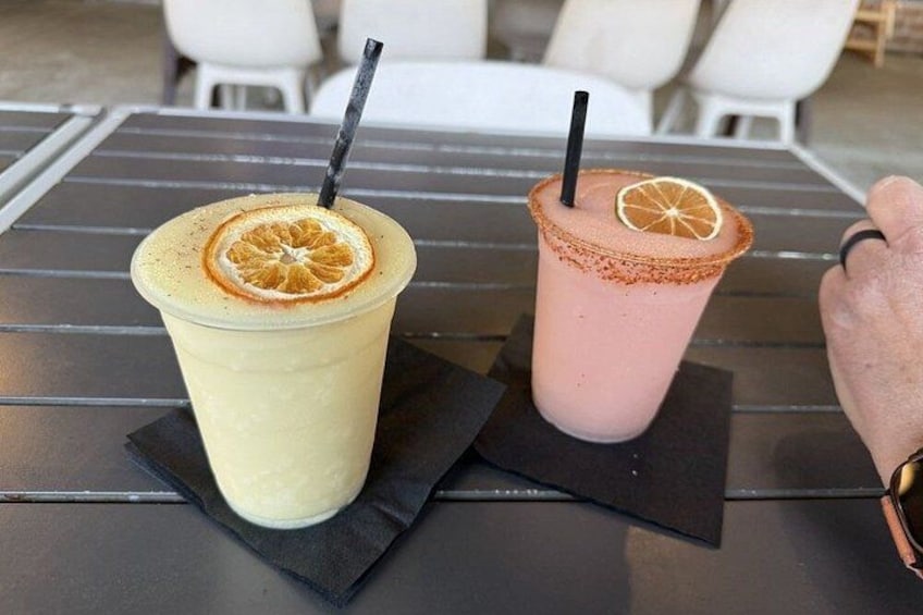 Two drinks on a table with a black rim, one with a lemon slice and the other with a strawberry slice. 2