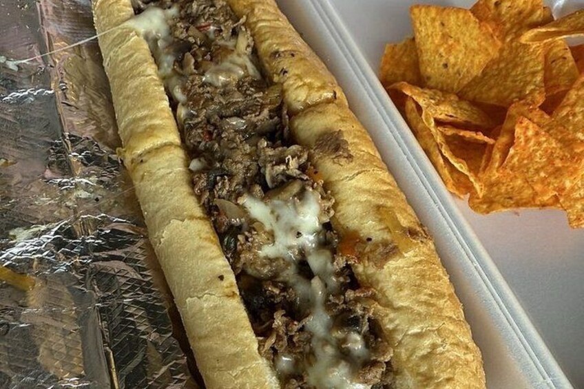 A sandwich with meat and cheese, and a container of chips. 2