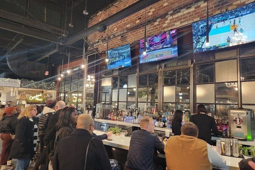 A bar with multiple screens, a crowd of people, and a brick wall. 4