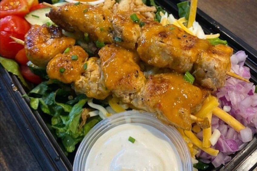 Skewers of grilled meat, salad, and a container of sauce. 3