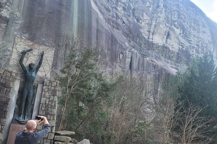 A person taking a photo of a statue against a rocky cliff. 5