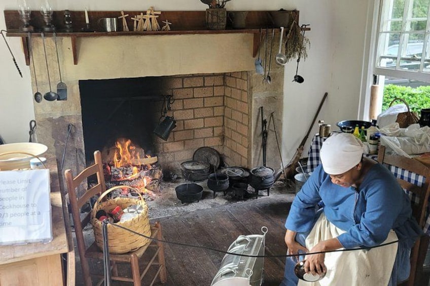 A chef cooking in a rustic kitchen with a brick fireplace, wooden utensils, and cooking pots. 2