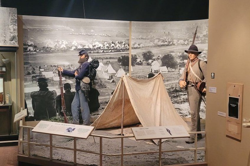A historical exhibit with a tent, two figures, and informational panels. 4