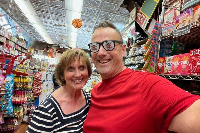 En person i en röd tröja tar en selfie i en butiksgång, med hyllor fulla av olika produkter. 2