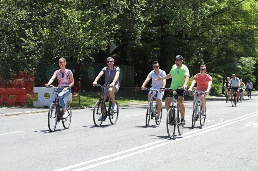 Een groep mensen fietst over een weg, met bomen en een hek op de achtergrond. 2