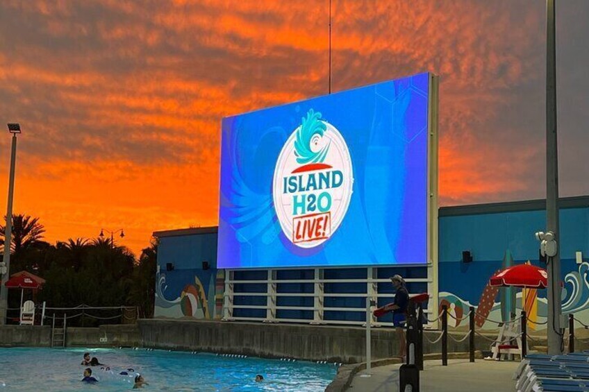 A large billboard advertising 'Island H2O Live!' with a pool and umbrellas in the foreground. 5