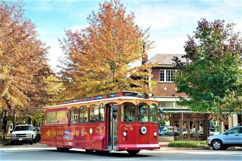 Un tramway rouge, portant l’inscription « GRIT LINE TOURS » sur le côté, est garé dans une rue bordée d’arbres aux couleurs automnales, avec un bâtiment visible au loin. 2