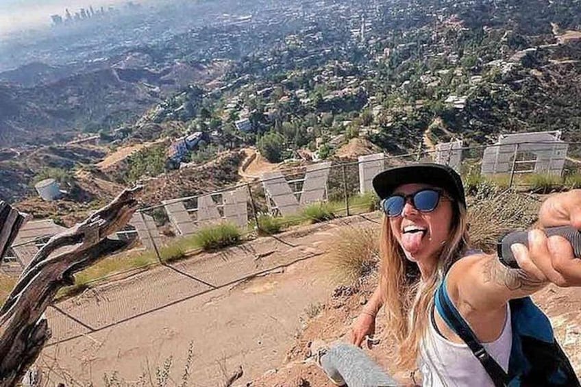 A person taking a selfie with a scenic view of a hilly landscape and a fence in the foreground. 4