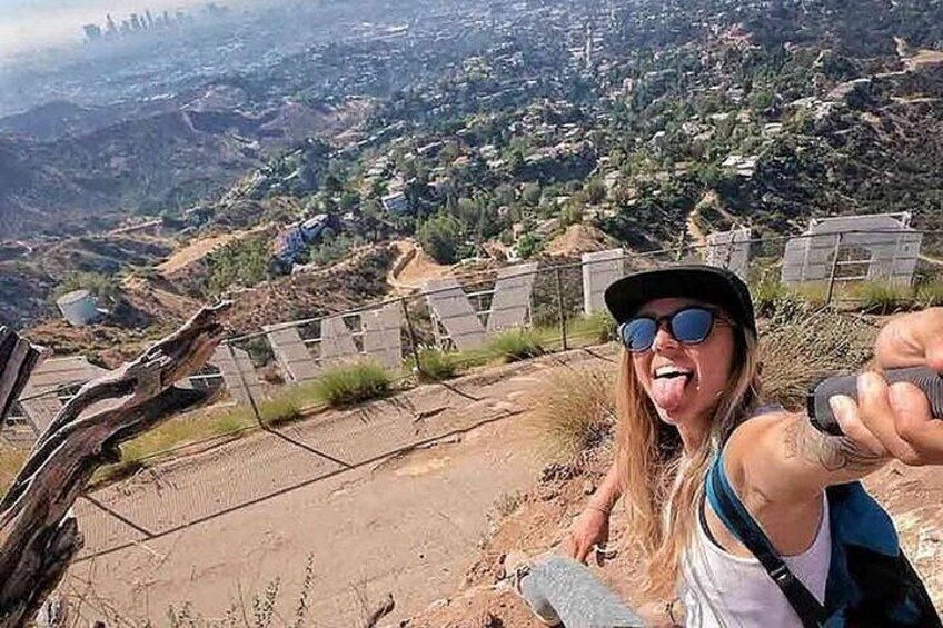A person taking a selfie with a scenic view of a hilly landscape and a fence in the foreground. 3