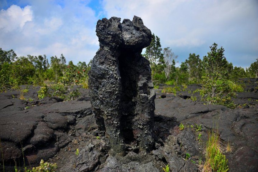 A volcanic rock formation with a central opening, surrounded by a landscape of sparse vegetation and trees. 3