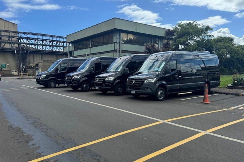 Een parkeerplaats met meerdere zwarte bestelwagens voor een gebouw met een metalen constructie. 4