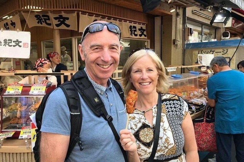 A man and a woman standing in front of a food stall with a sign in a foreign language. 3