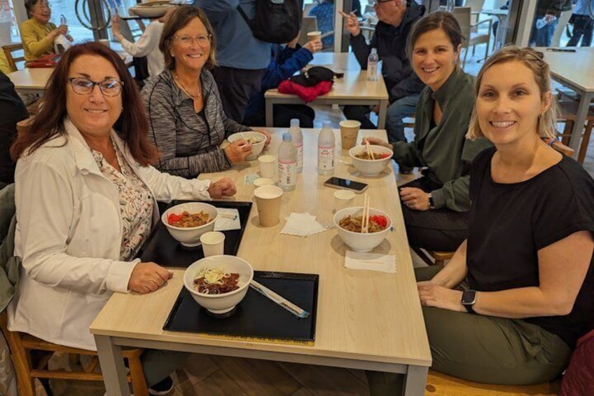 Cuatro personas sentadas en una mesa con platos de comida, un teléfono inteligente y una taza. 2
