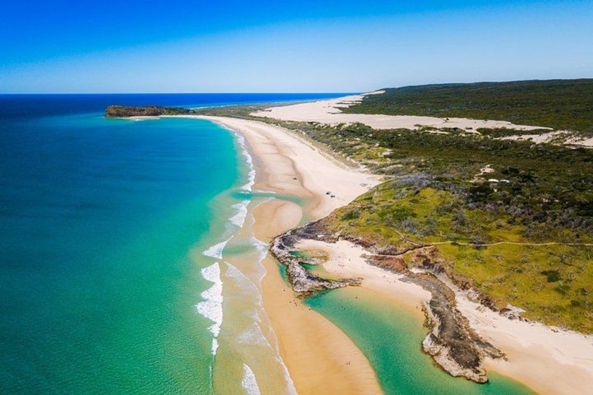 A coastal landscape with a sandy beach, turquoise waters, and green vegetation. 4