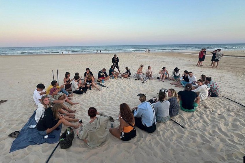Eine Gruppe von Personen sitzt im Kreis am sandigen Strand. 5