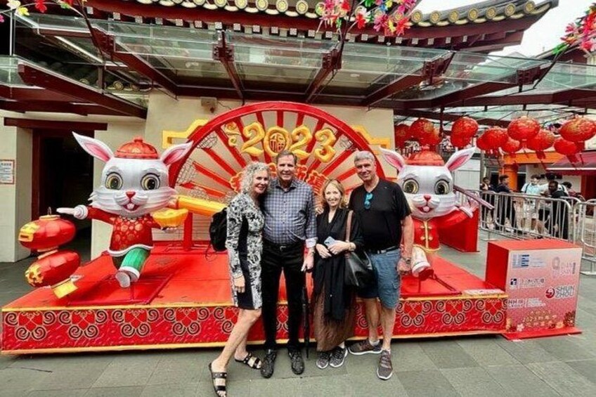 A group of people posing in front of a red and gold decorative structure with rabbit figures and a large number sign. 2