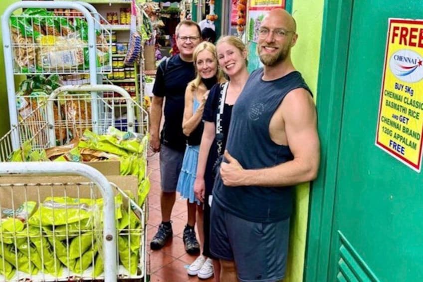 Eine Gruppe von Personen in einem Gang eines Supermarktes, ein Einkaufswagen mit grünen Taschen gefüllt. 2