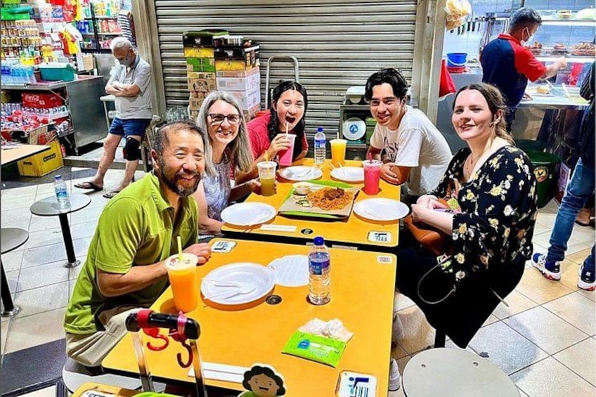Un gruppo di persone che cena in un caffè all'aperto, con tavoli, sedie e diversi piatti. 2