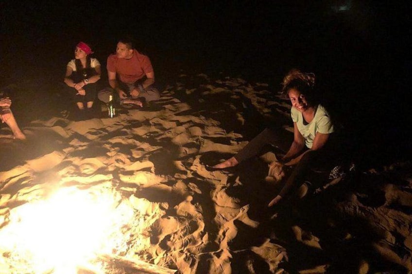 Mensen zitten 's nachts rond een kampvuur op een zandstrand. 2