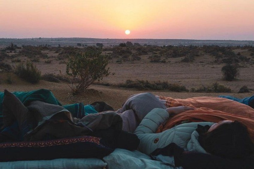 Iemand slaapt in bed met dekens, met op de achtergrond een woestijnlandschap bij zonsondergang. 1