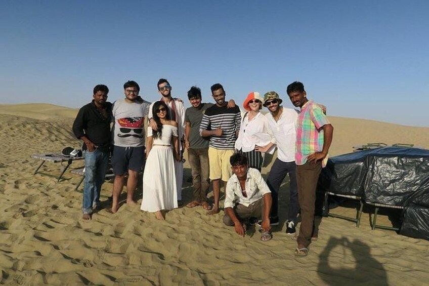 A group of people standing on a sandy beach with a tent and a table in the background. 4