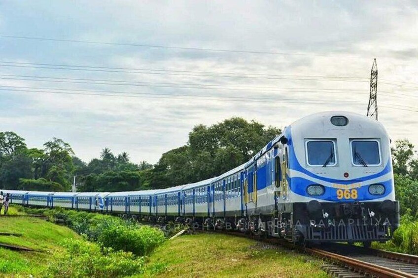A blue and white train numbered 968 on tracks with greenery and trees in the background. 1