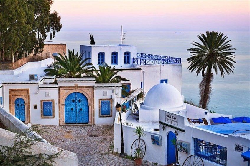 Un edificio costero con puertas y ventanas azules, una palmera y una vista despejada del mar. 5