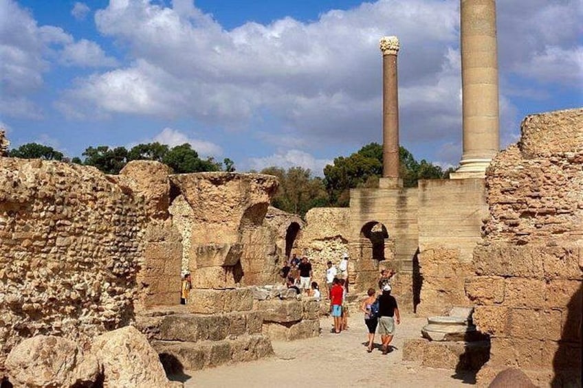Ruinas antiguas con columnas y arcos de piedra, visitantes caminando por el lugar. 1