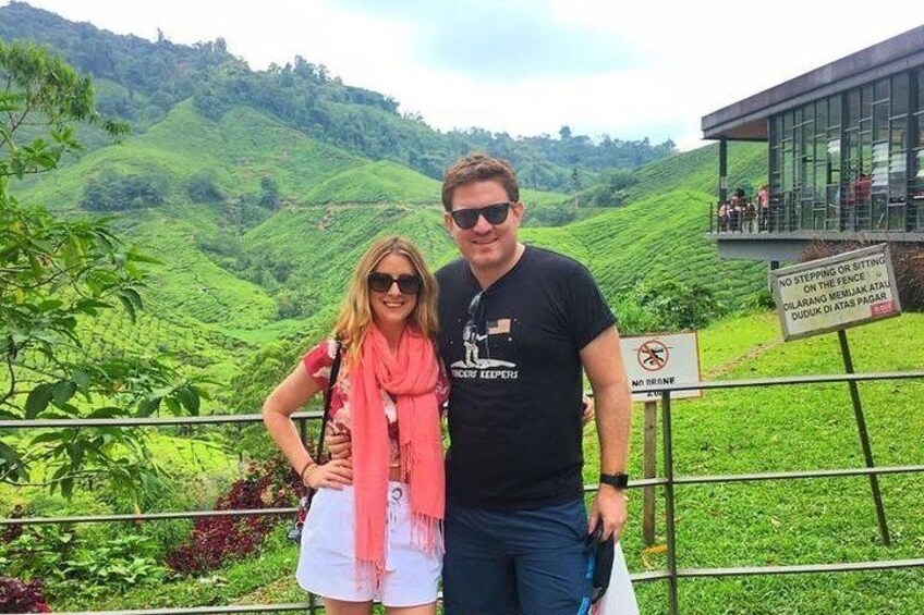 A couple standing in a lush green landscape with a sign indicating no stepping or sitting on the fence. 3