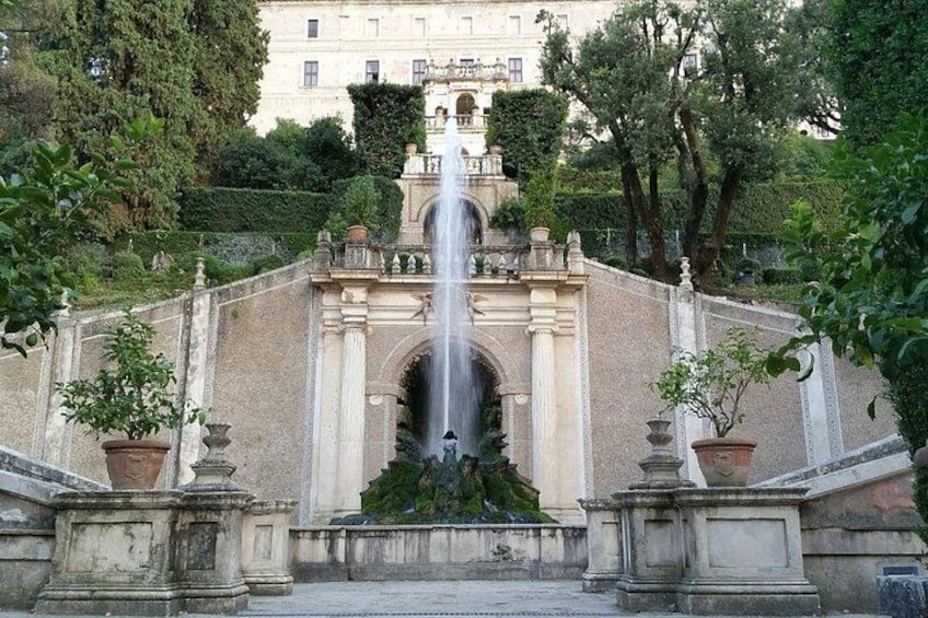 A grand fountain with water cascading down a stone structure, surrounded by classical architecture and lush greenery. 5