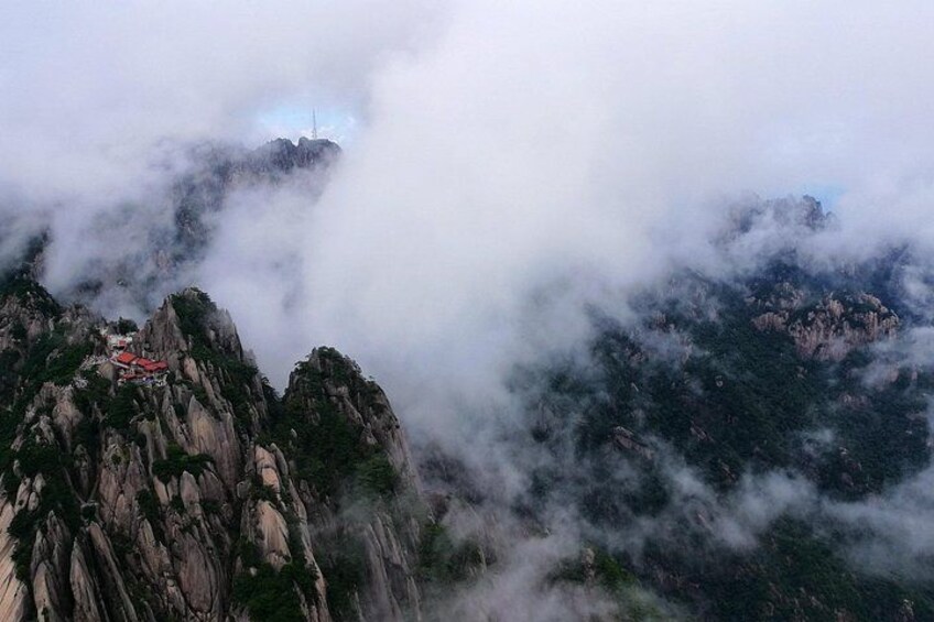 A mountainous landscape with rocky peaks, a red-roofed structure, and clouds enveloping the terrain. 5
