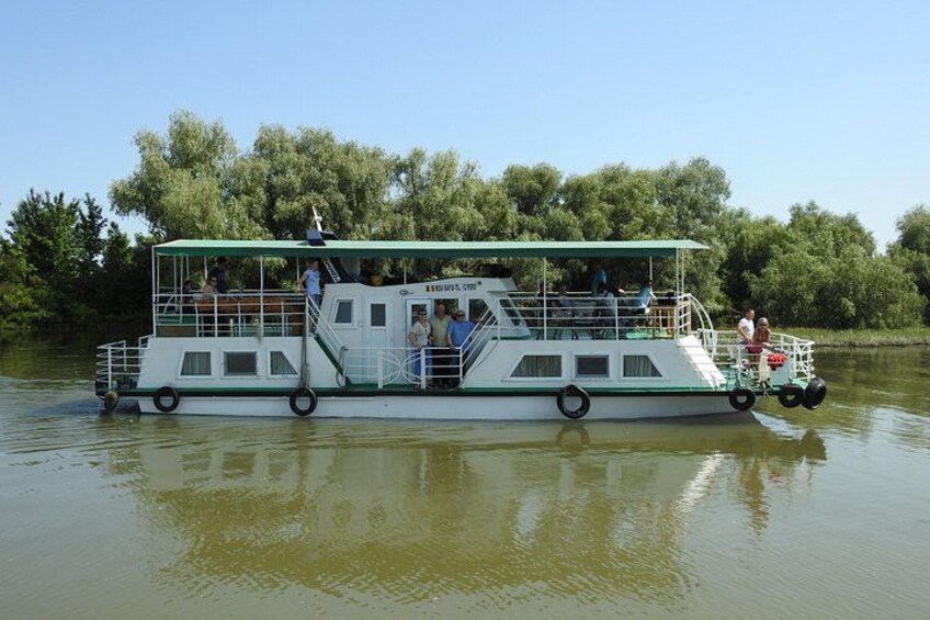 Een rivierboot met passagiers, omringd door bomen. 1