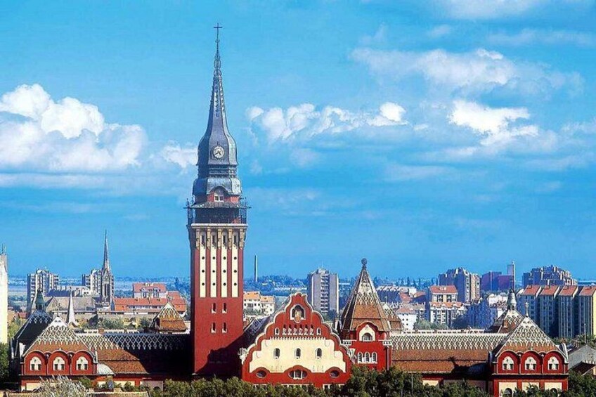 A cityscape with a prominent clock tower, a distinctive red building with a pointed roof, and a variety of other architectural styles. 1