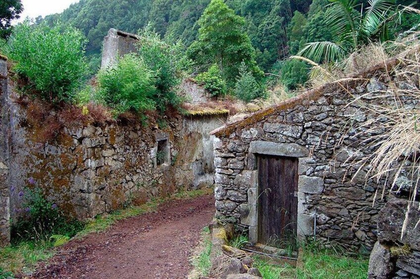 Un edificio rústico de piedra con puerta de madera, rodeado de abundante vegetación y un sendero de tierra. 2