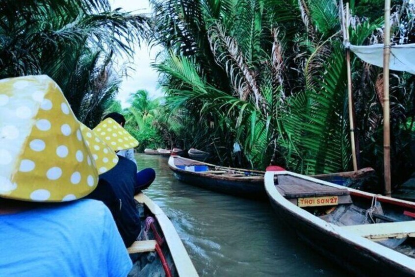 A narrow waterway with boats, dense tropical vegetation, and a person wearing a polka-dotted hat. 2