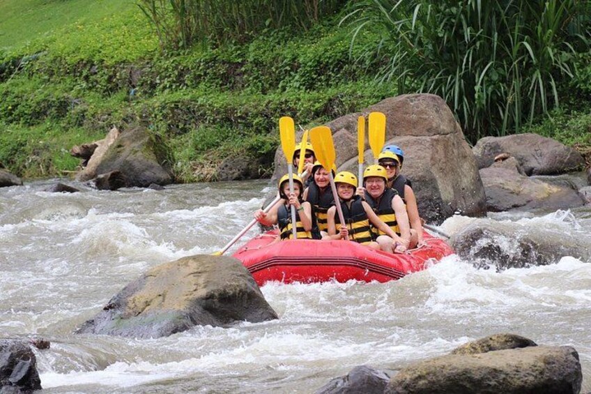 A group of people in a red raft navigating a river with rapids, surrounded by rocks and greenery. 3