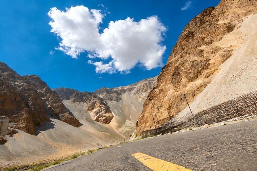 A mountainous landscape with a paved road, a yellow line, and a rocky cliff. 5
