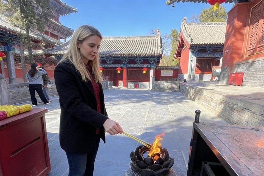 A person lighting incense sticks in a traditional courtyard with red buildings and tiled roofs. 4