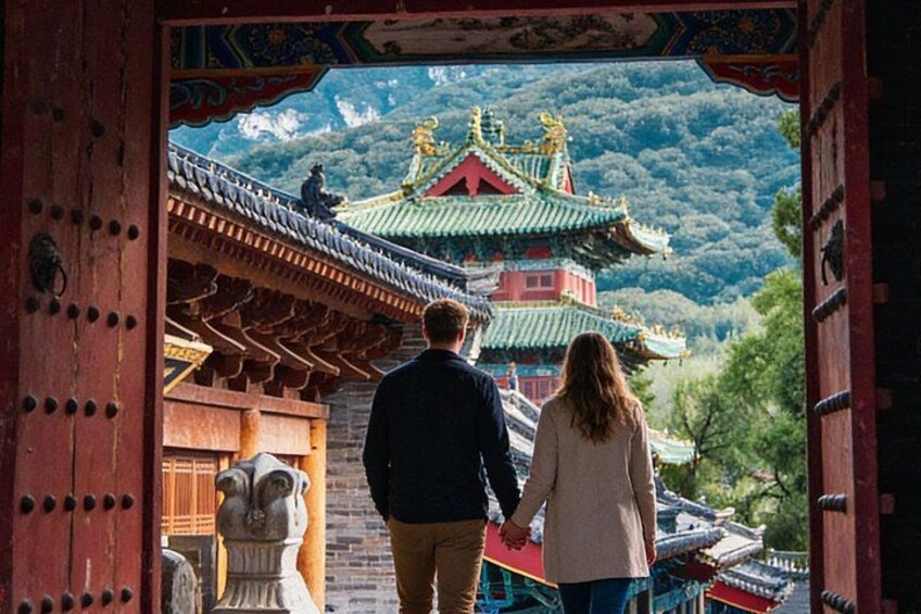 Een stel loopt door een traditioneel hek naar een meerlaagse pagode met versierde architectuur, met op de achtergrond weelderige groene bergen. 1