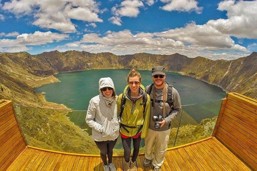 Three people standing on a wooden platform overlooking a lake surrounded by mountains. 1
