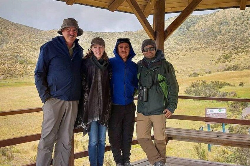 Four people standing on a wooden platform with a mountainous landscape in the background. 3