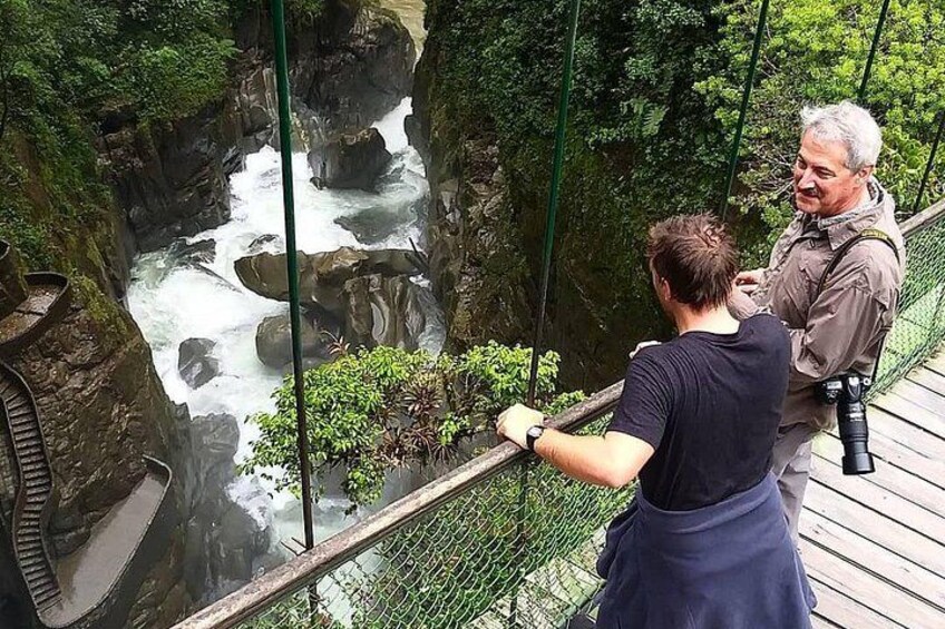 A person standing on a wooden bridge overlooking a river with rocks and greenery. 2