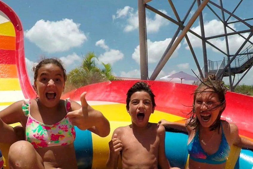 Trois personnes sur un toboggan aquatique aux couleurs vives, avec un ciel dégagé et des palmiers en arrière-plan. 5